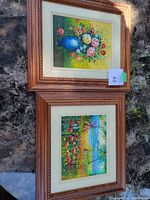 Pair of framed paintings viewed together showing floral and landscape artwork with carved wooden frames and white mats.