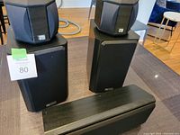 Photo showing the five speakers: two small bookshelf M2 speakers sitting on top of two larger Quadrant QS-8 surround speakers, and the VP50 centre speaker laid flat in front.