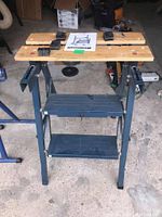 Front view of the Mastercraft folding work bench fully set up, showing wooden top panels and metal frame with cross supports.
