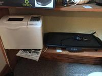 Photo showing side-by-side Black & Decker breadmaker and West Bend griddle on wooden shelf in a basement setting.