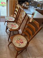 Three wooden ladder-back dining chairs with floral needlepoint round seat mats placed on tiled floor next to kitchen counter.
