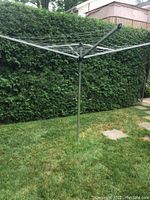 Full view of the Brabantia Topspinner folding clothesline set up outdoors on grass with a hedge background.