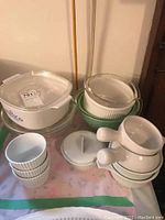 Photo of assorted Corning Ware baking dishes, bowls, cups, and lids organized on a table, showing variety in shapes and sizes.