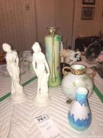 Group of decorative figurines and vases arranged on a quilted surface with background showing room setting