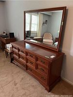 Front angle view of cherry wood dresser with attached large framed mirror, brass handles on drawers.