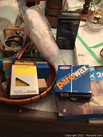 Wooden basket containing boxed glue sticks, wax bars, and small jewelry boxes on table surface