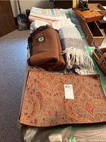 Six patterned placemats in paisley design, alpaca and wool reversible throw, and brown acrylic throw folded on a table.