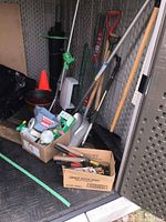 Photo showing snow shovels, garden pots, and other gardening tools leaning and stored in a small area or vehicle space.