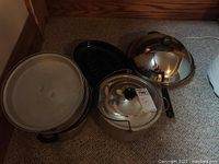 Wide shot showing assortment of pots and pans including stainless steel pots with lids and a grill pan.