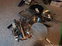 Full view showing assorted pots, strainers, pans, and utensils bundled together on floor.