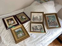 Six framed prints arranged on a bed, showing two rows of three prints each varying in frame and subject matter.