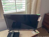 Front view of Samsung flatscreen TV with cable box and remote placed on table.