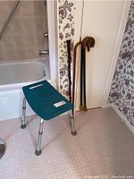 Photo showing shower chair positioned next to bathtub and four wooden canes leaning against wall