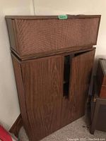 Front left view of one unit showing the top speaker enclosure with woven grill and closed bottom cabinet doors