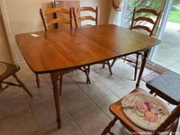 Photo of wood dining table set up with leaves and chairs around it, showing the overall condition and design.