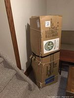 Two large cardboard boxes stacked containing the packed Christmas tree, with strings securing the boxes.