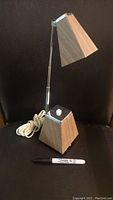 Full view of lamp showing wooden angled shade, adjustable metal arm, and wooden pyramid base with knob switch and power cord with Sharpie marker for size reference.