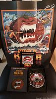 Collector's poster featuring a large angry tomato with sharp teeth attacking humans, along with title 'Attack of the Killer Tomatoes' and the DVD case displayed on chair.