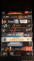 Stacked side view of 10 VHS sealed tapes showing titles and packaging condition.