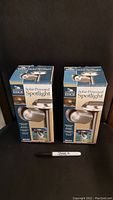 Two boxed Journey's Edge Solar-Powered Spotlights placed upright with a Sharpie for scale, both in new condition within sealed packaging.