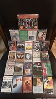 Front view showing all 25 sealed audio cassette tapes arranged in rows, showcasing various titles and artists with visible case labels and artwork.