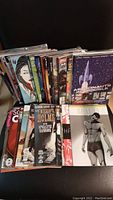 Photo of multiple comic books standing up showing various covers with graphic novel style artwork, starry sky and superhero themes.