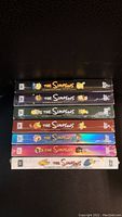 Seven sealed DVD box sets of The Simpsons arranged side by side showing the spines with colorful character art.
