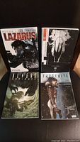 Lot of 4 graphic novels: Lazarus, Aliens Defiance, Frostbite, and a monochrome cover with a figure