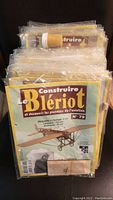 Stack of individually packaged Le Blériot model kits in plastic wrap, showing cover sheets with historical airplane drawings and instructions.