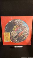 Full view of sealed Beatles Sgt. Pepper's Limited Edition Picture Disc with red outer cover and Sharpie pen for scale.