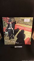 Front cover of Leonard Cohen "Old Ideas" album in original shrink wrap, showing Leonard Cohen sitting on a bench outside reading a book.
