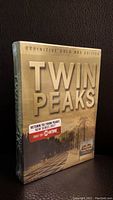 Front of the sealed Twin Peaks Definitive Gold Box Edition DVD set showing gold text and outdoor image.