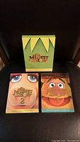 Front view of The Muppet Show Seasons 1-3 DVD box sets, showing colorful illustrations of Muppet characters. Box set 2 and 3 are sealed.