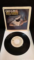 7-inch vinyl record sleeve featuring Gremlins artwork with hands opening a box containing a small creature, with title and artist name visible.
