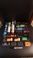 Entire collection of vintage Thomas the Tank Engine wooden toy trains and railway cars arranged on black chair, with a Sharpie pen included for scale.