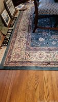 Partial view of the blue and cream area rug with floral patterns, laid out on a hardwood floor under a dining chair.