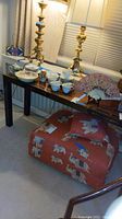 Full view of black lacquered Asian style sofa table with various items on top and an upholstered ottoman with elephant design underneath
