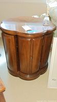 Front view of the dark brown wooden side table cabinet showing the panel details on the curved sides and the clover-shaped top surface.