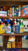 Shelf with assorted cleaning sprays (Lysol, Clorox Tilex, Fantastik), Brillo soap pads box, Downy dryer sheets, and other cleaning products.