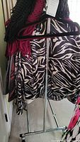 Photo showing clothing rack holding a zebra-patterned garment on a black hanger and some clothing items above it.