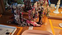 Wide shot showing multiple costume jewelry necklaces hanging on three figural jewelry display stands resembling women's legs dressed in various outfits.