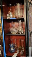 Photo showing multiple glass and crystal vases of varying shapes and sizes on a display shelf, including cut crystal and smooth glass with swirl patterns, and a small blue-accented glass item.