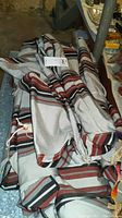 Folded and rolled pieces of striped cloth fabric with red, white, black, and grey stripes, presumably for an awning.