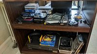 Image shows shelves containing a portable DVD player, a JVC VCR, CDs, DVDs, earphones, and additional electronic devices.