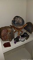 Display of rough and sliced geodes including a large sliced blue-gray geode on wooden tripod stand with smaller amethyst clusters around it.