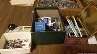 Box with assorted small metal findings, clips, pins, and several fountain pens and ink bottles.