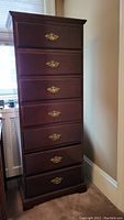 Front view of tall wooden 7 drawer lingerie chest in dark polished wood with brass metal handles.