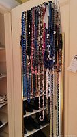 Wide view of all hanging costume jewelry necklaces on door rack showing variety of colors and bead types.
