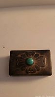 Top view of rectangular silver pill box showing floral design and central turquoise stone on lid.