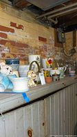 Shelf with a variety of ceramic pots, planters, glass vases, and decorative animal figurines against a brick wall in a basement area.